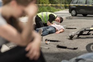 Man in hi-vis vest giving first aid to accident victim on road with debris, distress in foreground โ urgent post-crash scene