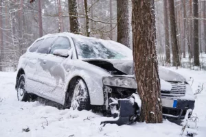 Damaged white car crashed into tree in snowy Alabama forest, illustrating collision risks during ice storms and challenges in proving negligence versus weather-related accidents.