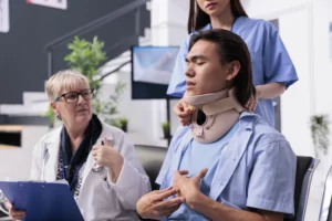 Young man in neck brace at clinic with nurse and doctor, illustrating medical evaluation after an accident in Alabama.