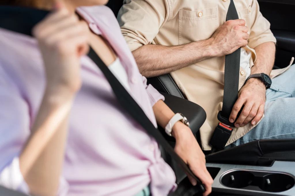 Two people fastening seat belts in a car, illustrating safety and legal compensation questions when not wearing a seatbelt after an Alabama accident.