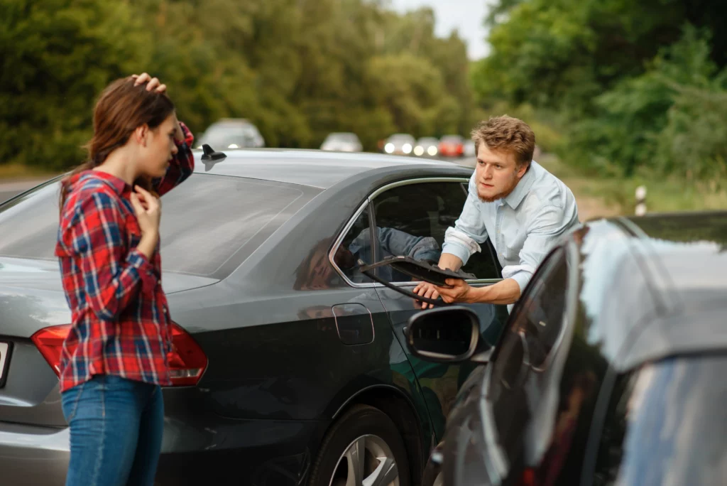 Man leaning out of car window showing bumper damage to concerned woman after a minor collision on a forest road, illustrating deciding if you need a lawyer for a minor car accident in Alabama.