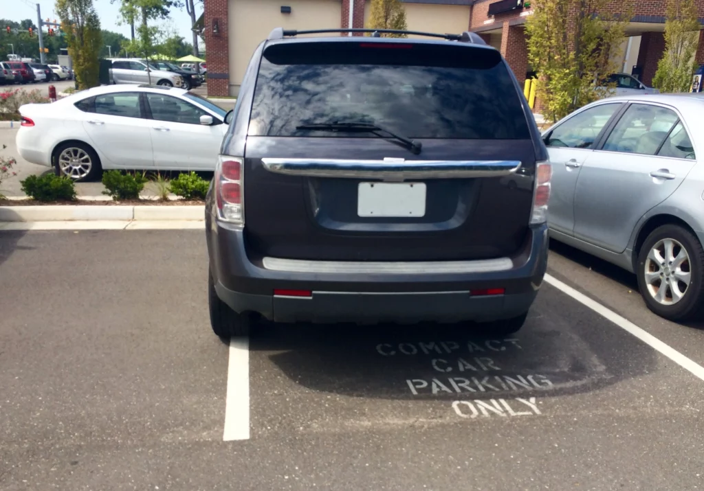 Large SUV parked in a compact-only space in a crowded parking lot, illustrating potential liability and hazards leading to parking lot accidents in Alabama.