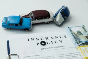 Toy cars involved in a collision above an insurance policy with cash nearby, illustrating a denied car accident insurance claim and financial consequences.