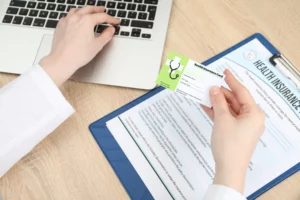 Person at a desk holding a health insurance card and using a laptop with an insurance form, illustrating concerns about insurers accessing medical records without permission.
