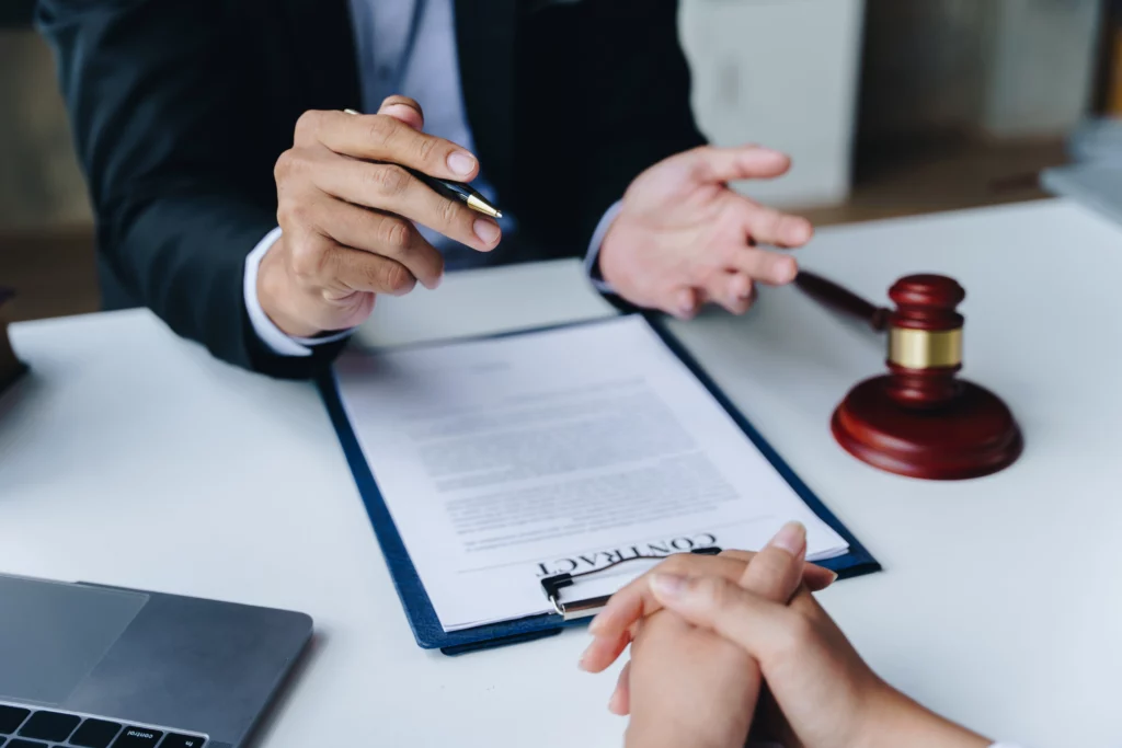 Attorney pointing to a contract on a desk beside a gavel while discussing case details with a client, representing the evaluation of damages, liability, and factors that determine how much a personal injury case may be worth in Alabama.