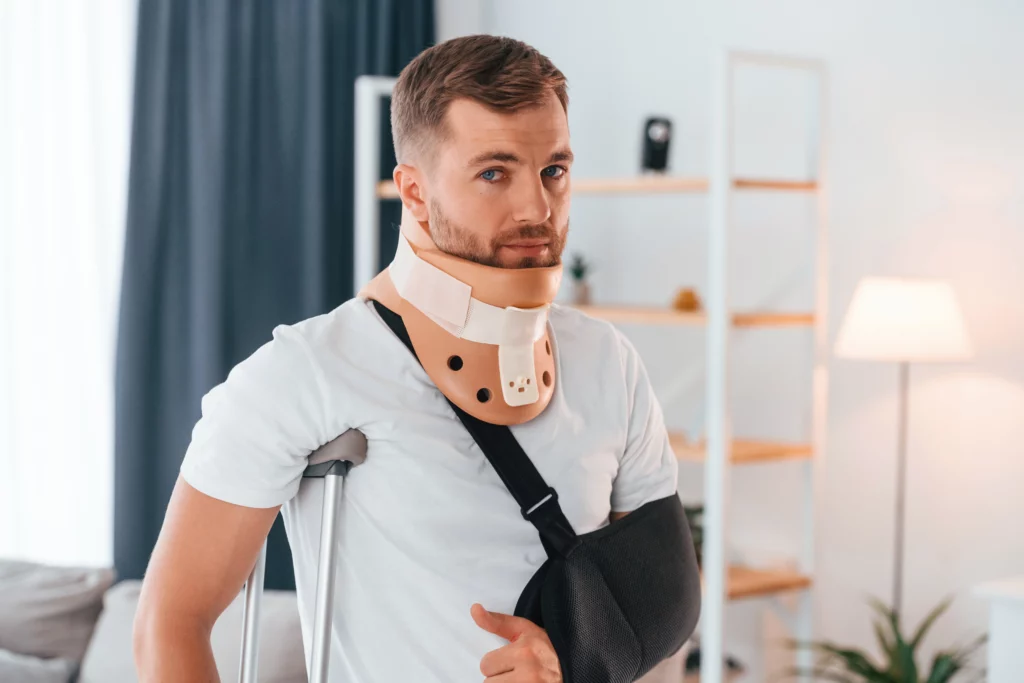 Man wearing a neck brace and arm sling sitting at home with crutches nearby, representing the recovery process and potential legal rights after sustaining injuries on someone else’s property in Alabama premises liability cases.